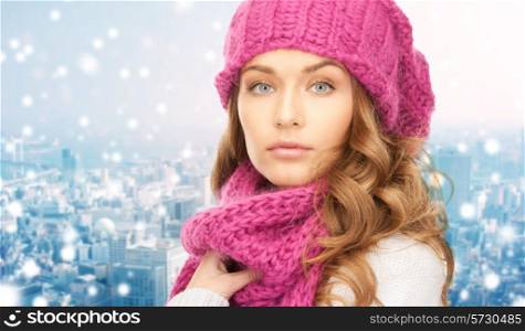 happiness, winter holidays, christmas and people concept - close up of young woman in pink hat and scarf over blue snowy background