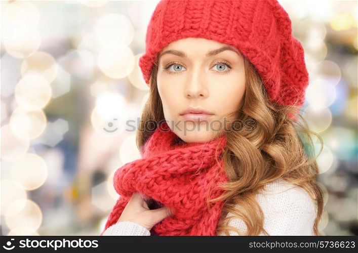 happiness, winter holidays, christmas and people concept - close up of young woman in red hat and scarf over lights background
