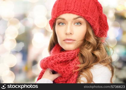 happiness, winter holidays, christmas and people concept - close up of young woman in red hat and scarf over lights background