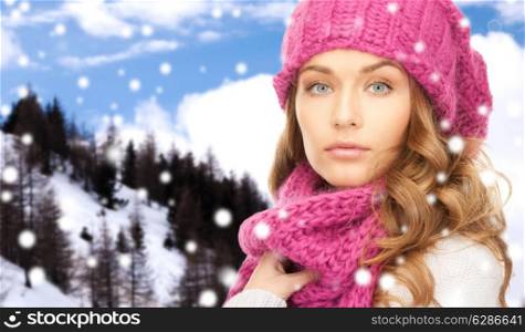 happiness, winter holidays, christmas and people concept - close up of young woman in pink hat and scarf over snowy mountains background
