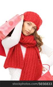 happiness, winter holidays, christmas and people concept - smiling young woman in red hat, scarf and mittens carrying shopping bags over white background
