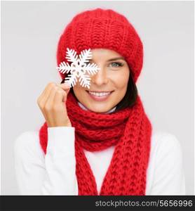 happiness, winter holidays, christmas and people concept - smiling young woman in red hat, scarf and mittens covering one eye with snowflake decoration over gray background