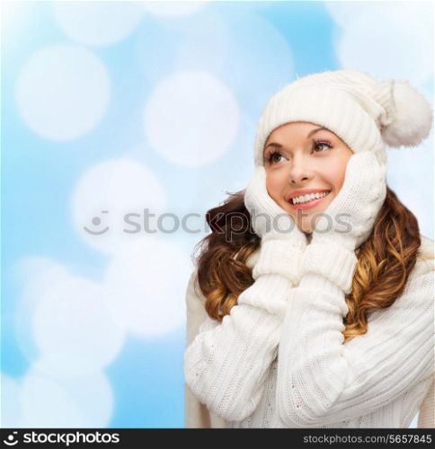 happiness, winter holidays, christmas and people concept - smiling young woman in white hat and mittens over blue lights background