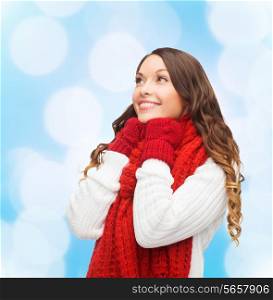 happiness, winter holidays, christmas and people concept - smiling young woman in red scarf and mittens over blue lights background