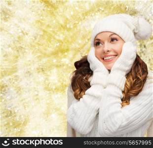 happiness, winter holidays, christmas and people concept - smiling young woman in white hat and mittens over yellow lights background