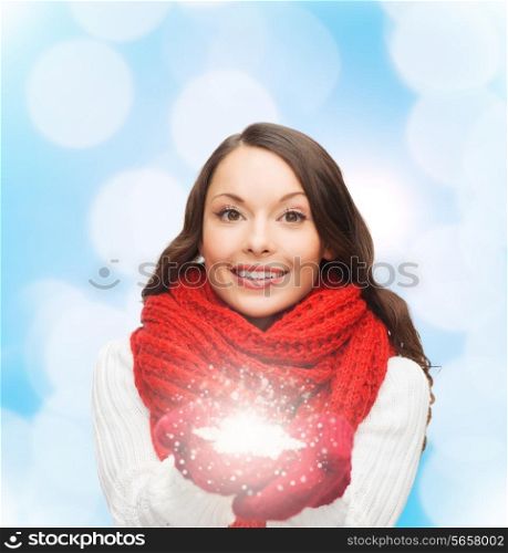 happiness, winter holidays, christmas and people concept - smiling young woman in red scarf and mittens holding snowflake over blue lights background