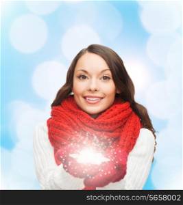happiness, winter holidays, christmas and people concept - smiling young woman in red scarf and mittens holding snowflake over blue lights background