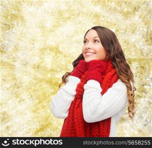 happiness, winter holidays, christmas and people concept - smiling young woman in red scarf and mittens over yellow lights background