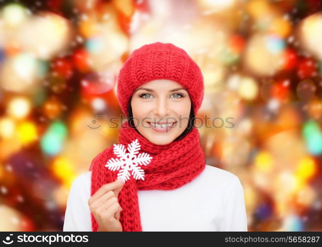 happiness, winter holidays, christmas and people concept - smiling young woman in red hat, scarf and mittens holding snowflake over red lights background