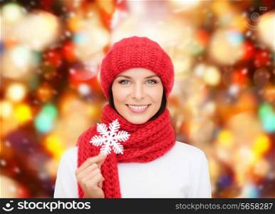 happiness, winter holidays, christmas and people concept - smiling young woman in red hat, scarf and mittens holding snowflake over red lights background