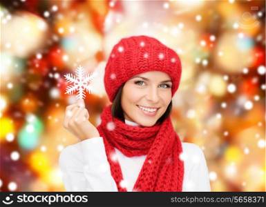 happiness, winter holidays, christmas and people concept - smiling young woman in red hat, scarf and mittens holding snowflake over red lights background