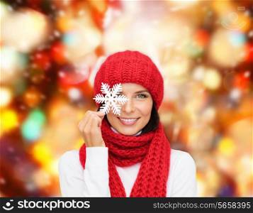 happiness, winter holidays, christmas and people concept - smiling young woman in red hat, scarf and mittens over holding snowflake red lights background