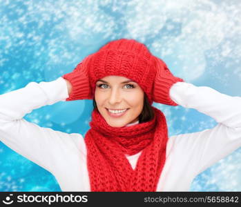 happiness, winter holidays, christmas and people concept - smiling young woman in red hat, scarf and mittens over blue snowy background