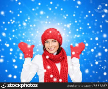 happiness, winter holidays, christmas and people concept - smiling young woman in red hat, scarf and mittens over blue snowy background