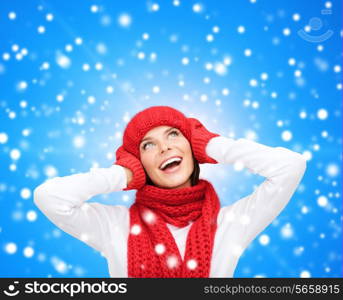 happiness, winter holidays, christmas and people concept - smiling young woman in red hat, scarf and mittens over blue snowy background