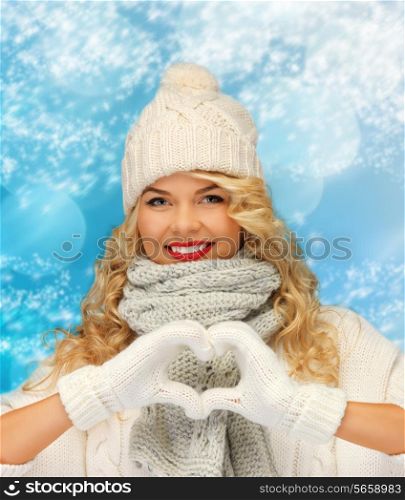 happiness, winter holidays, christmas and people concept - smiling young woman in white hat and mittens showing heart-shape gesture over blue snowy background