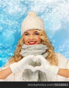 happiness, winter holidays, christmas and people concept - smiling young woman in white hat and mittens showing heart-shape gesture over blue snowy background