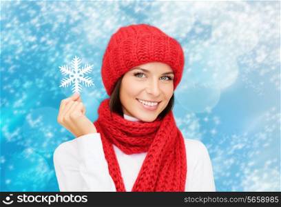 happiness, winter holidays, christmas and people concept - smiling young woman in red hat, scarf and mittens holding snowflake over blue lights background
