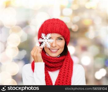 happiness, winter holidays, christmas and people concept - smiling young woman in red hat, scarf and mittens holding snowflake over lights background
