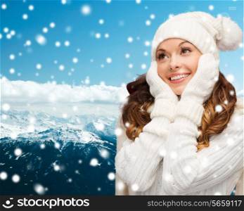 happiness, winter holidays, christmas and people concept - smiling young woman in white hat and mittens over blue snowy mountains background