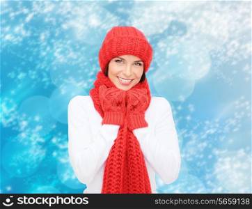 happiness, winter holidays, christmas and people concept - smiling young woman in red hat, scarf and mittens over blue snowy background