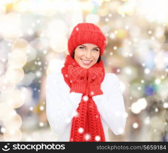 happiness, winter holidays, christmas and people concept - smiling young woman in red hat, scarf and mittens over lights background