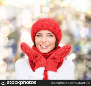happiness, winter holidays, christmas and people concept - smiling young woman in red hat, scarf and mittens over lights background
