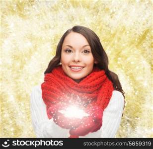 happiness, winter holidays, christmas and people concept - smiling young woman in red scarf and mittens holding snowflake over yellow lights background