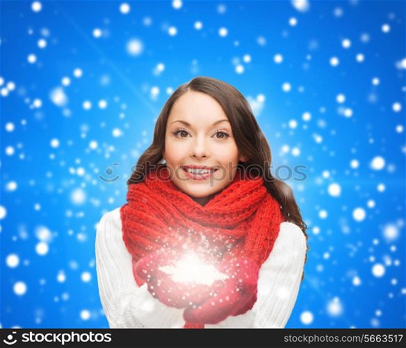 happiness, winter holidays, christmas and people concept - smiling young woman in red scarf and mittens holding snowflake over blue snowy background