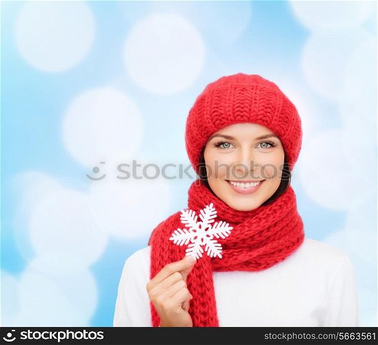 happiness, winter holidays, christmas and people concept - smiling young woman in red hat, scarf and mittens holding snowflake over blue lights background