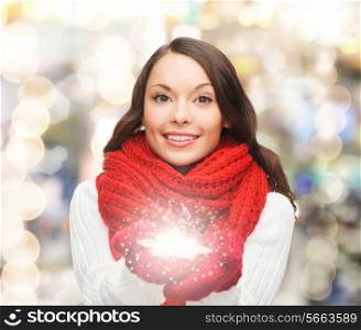 happiness, winter holidays, christmas and people concept - smiling young woman in red scarf and mittens holding snowflake over lights background