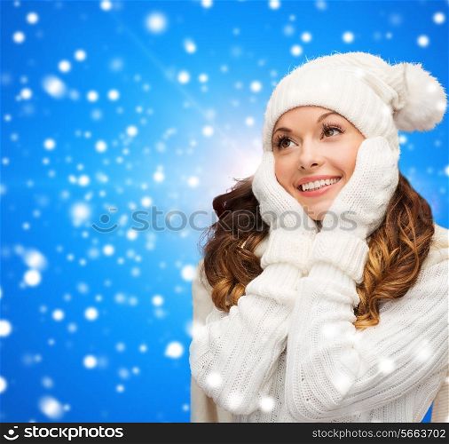 happiness, winter holidays, christmas and people concept - smiling young woman in white hat and mittens over blue snowy background