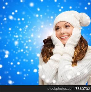 happiness, winter holidays, christmas and people concept - smiling young woman in white hat and mittens over blue snowy background