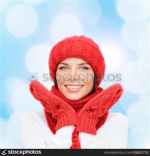 happiness, winter holidays, christmas and people concept - smiling young woman in red hat, scarf and mittens over blue lights background