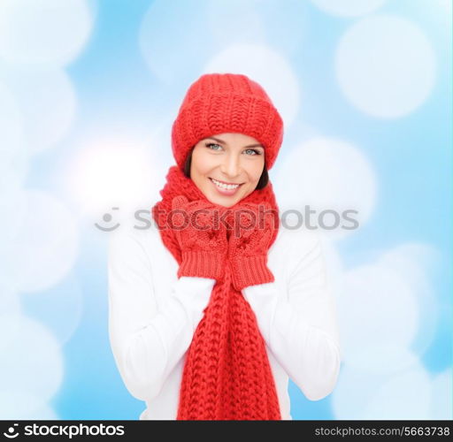 happiness, winter holidays, christmas and people concept - smiling young woman in red hat, scarf and mittens over blue lights background