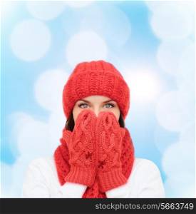 happiness, winter holidays, christmas and people concept - smiling young woman in red hat, scarf and mittens over blue lights background