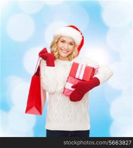 happiness, winter holidays, christmas and people concept - smiling young woman in santa helper hat with gifts and shopping bag over blue lights background