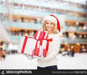 happiness, winter holidays, christmas and people concept - smiling young woman in santa helper hat with gifts over shopping center background