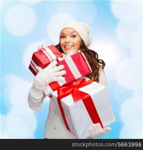 happiness, winter holidays, christmas and people concept - smiling young woman in santa helper hat with gifts over blue lights background