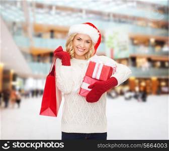 happiness, winter holidays, christmas and people concept - smiling young woman in santa helper hat with gifts and shopping bag over mall background