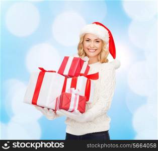 happiness, winter holidays, christmas and people concept - smiling young woman in santa helper hat with gifts over blue lights background