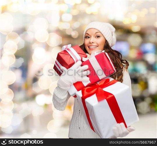 happiness, winter holidays, christmas and people concept - smiling young woman in santa helper hat with gifts over lights background