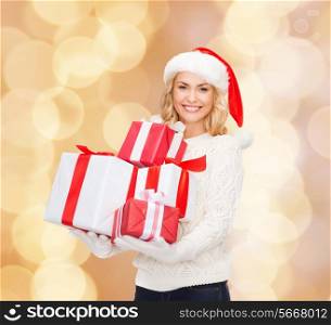 happiness, winter holidays, christmas and people concept - smiling young woman in santa helper hat with gifts over beige lights background