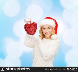 happiness, winter holidays, christmas and people concept - smiling young woman in santa helper hat with red heart decoration over blue lights background