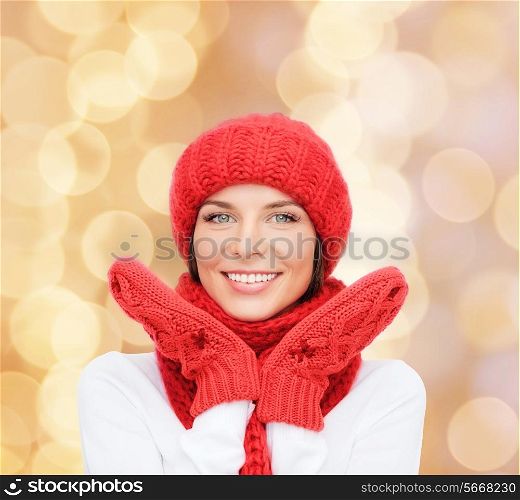 happiness, winter holidays, christmas and people concept - smiling young woman in red hat, scarf and mittens over beige lights background