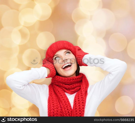 happiness, winter holidays, christmas and people concept - smiling young woman in red hat, scarf and mittens over beige lights background