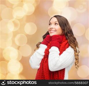 happiness, winter holidays, christmas and people concept - smiling young woman in red scarf and mittens over beige lights background