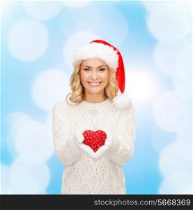 happiness, winter holidays, christmas and people concept - smiling young woman in santa helper hat with red heart decoration over blue lights background