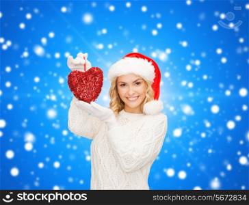 happiness, winter holidays, christmas and people concept - smiling young woman in santa helper hat with red heart decoration over blue snowy background