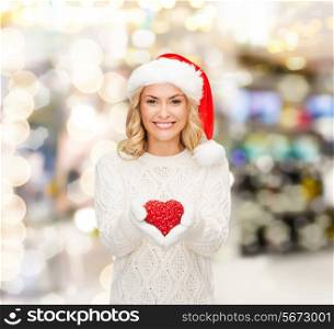 happiness, winter holidays, christmas and people concept - smiling young woman in santa helper hat with red heart decoration over lights background